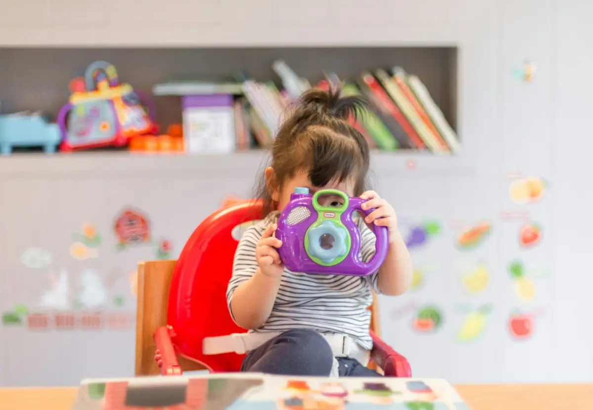 Niña jugando con una cámara de juguete en un aula colorida